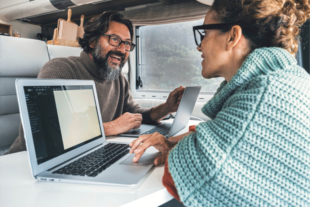 Zwei Personen arbeiten mit Laptops im Camper, Symbol für ortsunabhängiges Arbeiten und Selbstbestimmung.