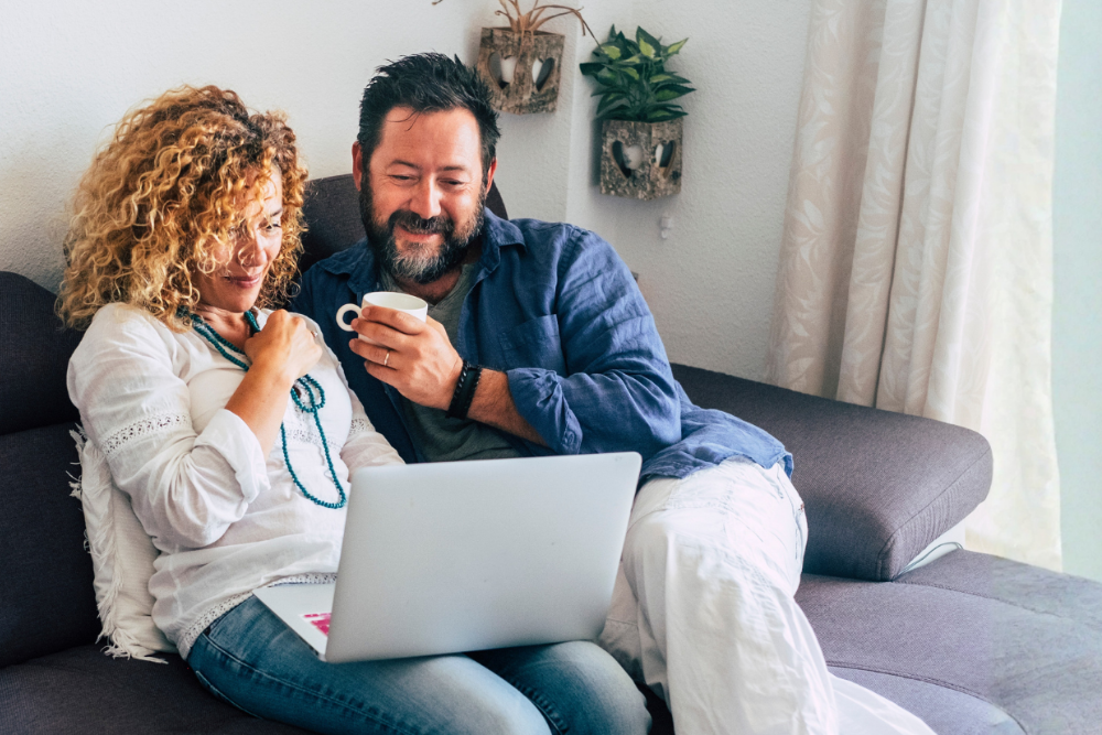 Paar sitzt entspannt auf einem Sofa mit Laptop, Symbol für flexibles Arbeiten von zuhause.