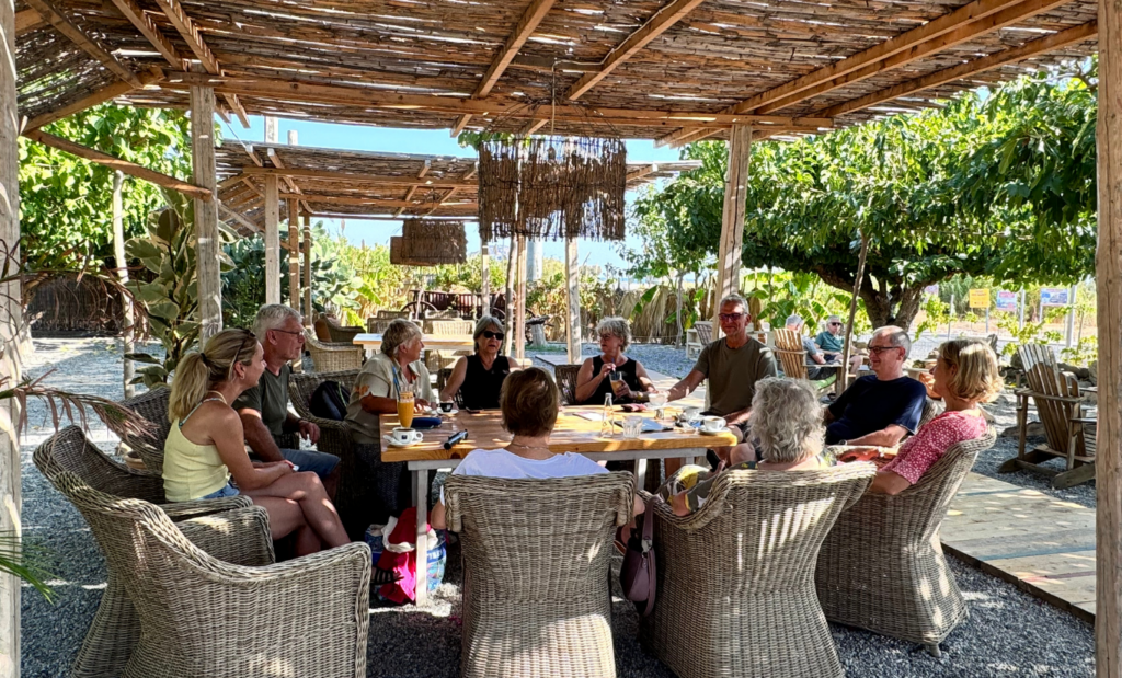 Gruppe von Erwachsenen sitzt gemeinsam an einem Tisch im Freien, Symbol für Austausch und Gemeinschaft.