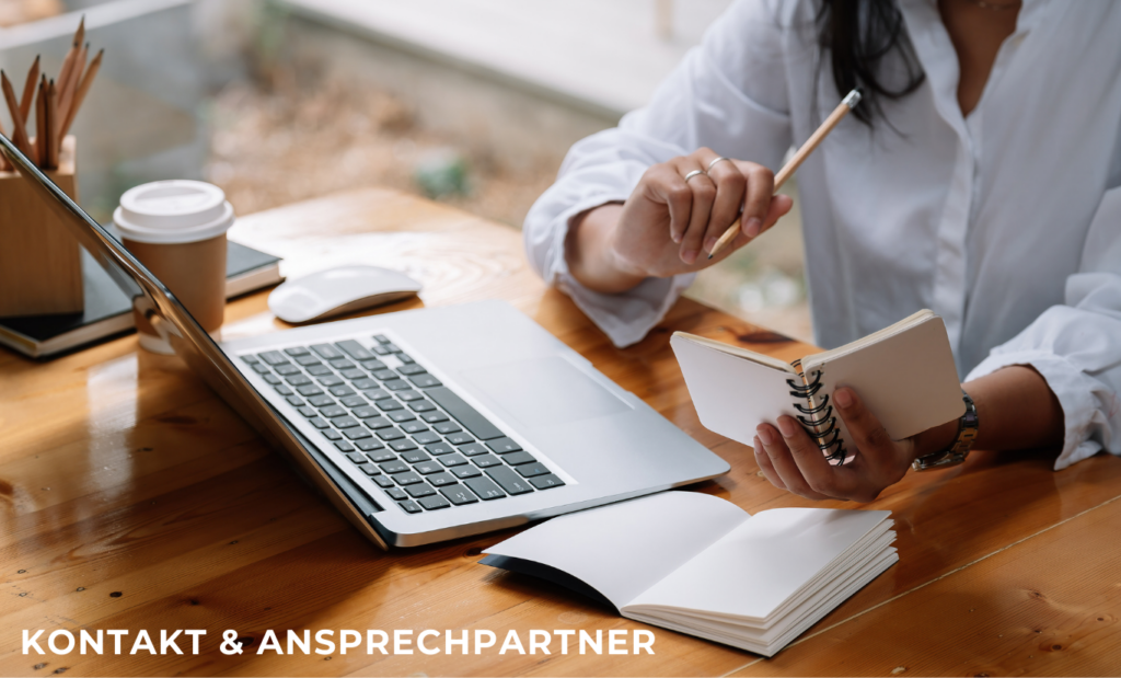 Person arbeitet am Laptop mit Notizbuch auf einem Tisch, im Bild steht „Kontakt & Ansprechpartner“.