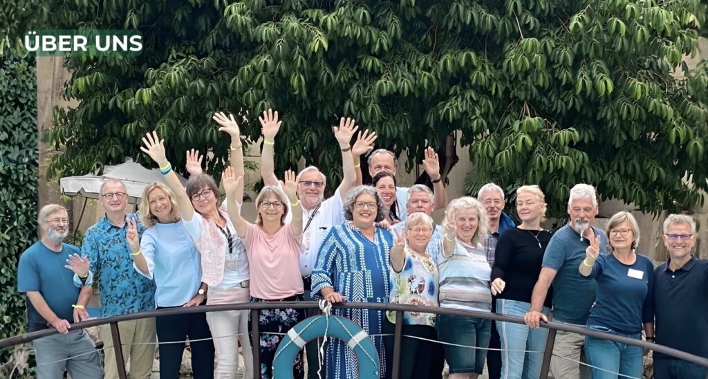 Team aus Frauen und Männern unterschiedlicher Altersgruppen steht gemeinsam im Freien und hebt die Hände.
