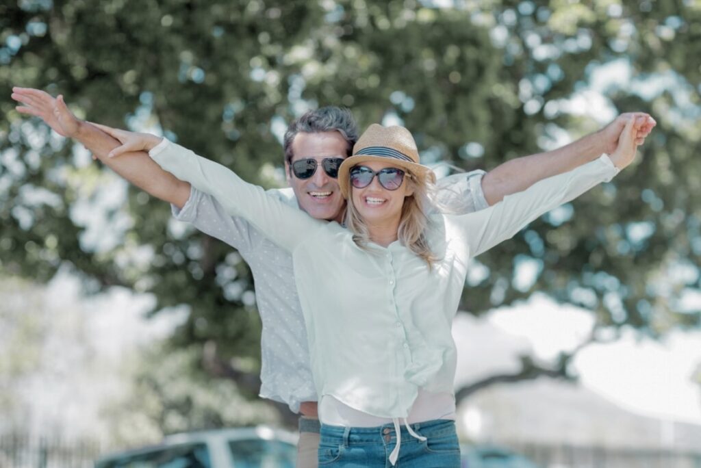 Lachendes Paar im Freien mit ausgebreiteten Armen, Symbol für Vitalität und Lebensqualität.